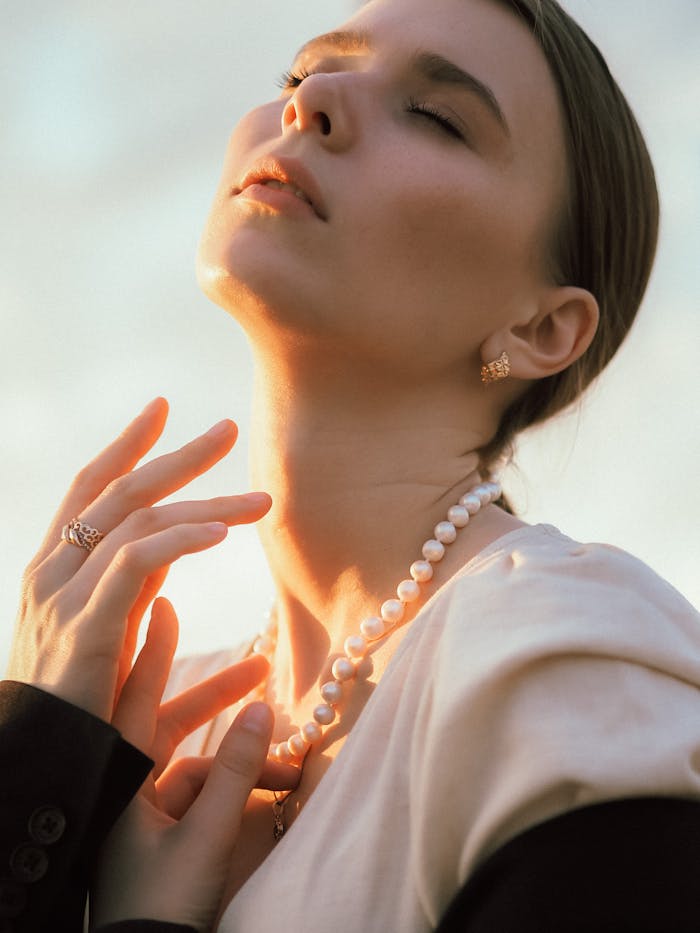 A serene portrait of a woman with closed eyes and pearl jewelry, basking in sunlight.